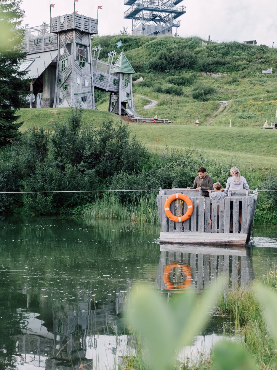 Familie fährt auf Floß über Geistersee mit Geisterschloss im Hintergrund