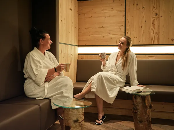 Zwei Frauen in Bademänteln entspannen mit Tee in einer Holz-Wellnesslounge