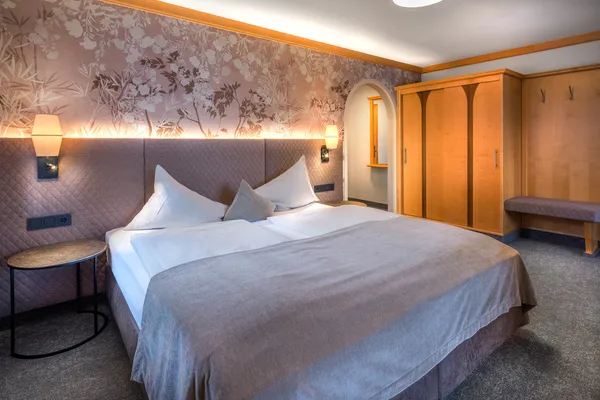 Gemütliches Hotelzimmer mit Doppelbett, Blumenwand und Kleiderschrank aus Holz