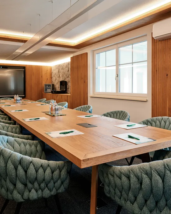 Moderner Konferenzraum mit Holztisch, stilvollen Stühlen und großem Präsentationsbildschirm