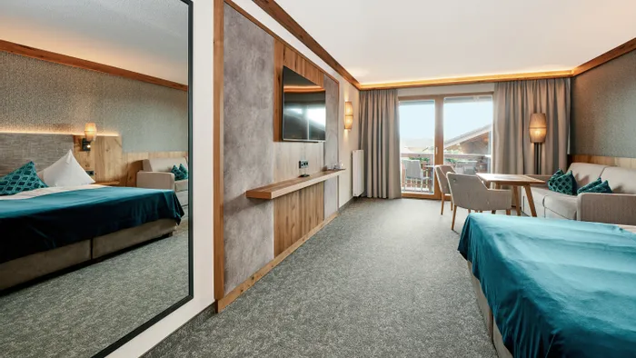 Modern hotel room with double bed, TV, sofa, balcony access and natural wood accents