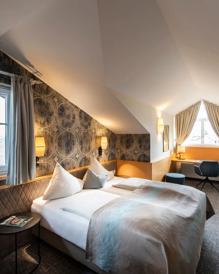 Cozy attic hotel room with double bed, desk, patterned wallpaper and large windows