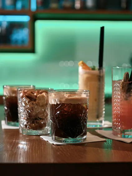 Verschiedene Cocktails in strukturierten Gläsern auf Bartheke mit grünem Neonlicht