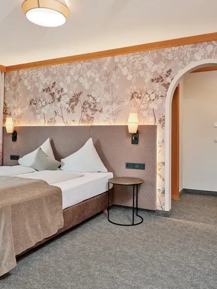 Gemütliches Hotelzimmer mit Doppelbett, Blumenmuster-Tapete und sanfter Beleuchtung