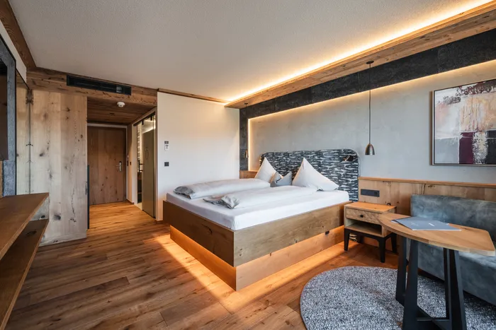 Camera d'albergo moderna con arredi in legno, letto matrimoniale, luci soffuse e area salotto accogliente