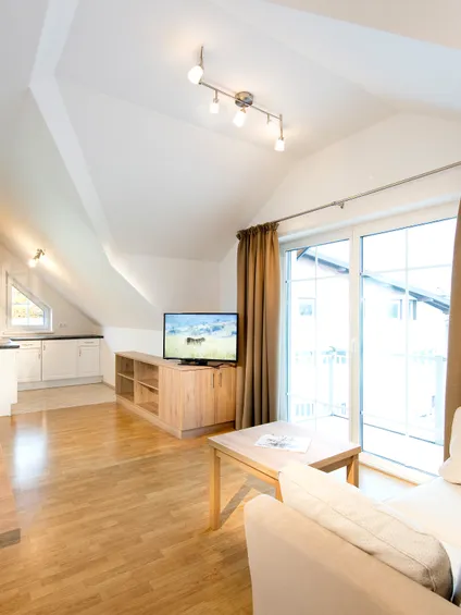 Helles Dachgeschoss-Wohnzimmer mit beigem Sofa, Holzboden und offener Küche