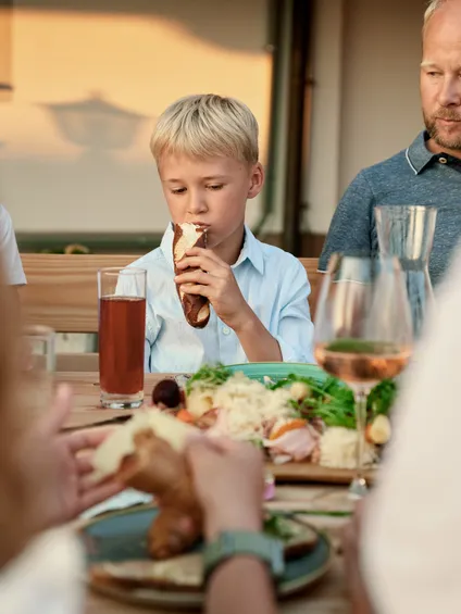 Junge isst Brezelsandwich beim Familienessen im Freien mit traditionellem deutschen Essen
