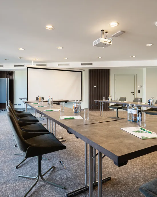 Moderner Konferenzraum mit U-förmigem Tischaufbau, Beamer, Flipcharts und natürlichem Licht