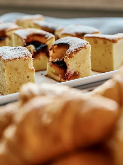 Vassoio di soffici fette di torta alle prugne con zucchero a velo accanto a croissant sfocati