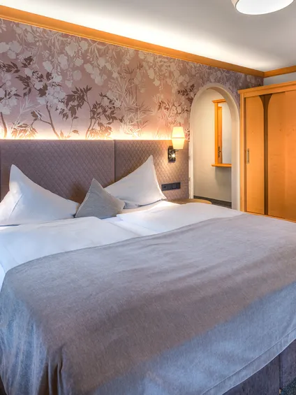 Gemütliches Hotelzimmer mit Doppelbett, Blumenwand und Kleiderschrank aus Holz