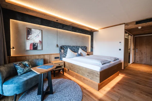 Modernes Hotelzimmer mit Holzboden, großem Bett, blauer Couch und warmer Ambientebeleuchtung