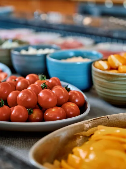 Frische Cherrytomaten und geschnittenes Gemüse in Schüsseln an einer bunten Salatbar