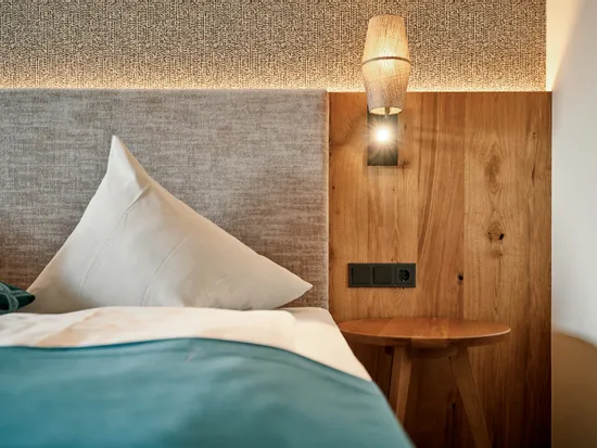 Gemütliches Hotelbett mit türkiser Bettwäsche, Holznachttisch und Wandleuchte