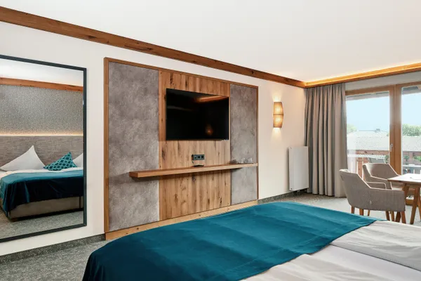 Modern hotel room with double bed, wood panel TV wall, and balcony access