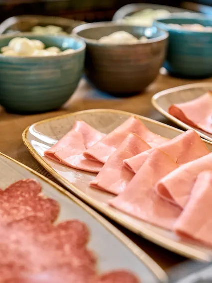 Verschiedene Aufschnittsorten wie Schinken und Salami auf Servierplatten am Frühstücksbuffet