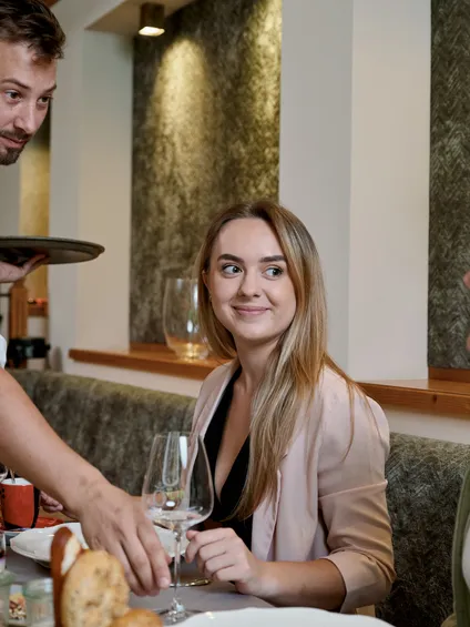 Kellner serviert Getränke an zwei Frauen an einem Restauranttisch mit Essen und Blumen