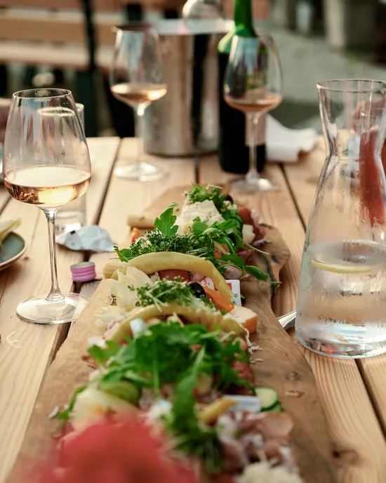 Essen im Freien mit Wurstplatte, Weingläsern und Personen beim Genießen des Essens