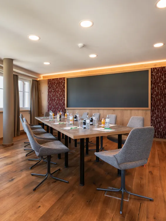 Moderner Konferenzraum mit Holzboden, großem Tisch, Stühlen und Flaschengetränken