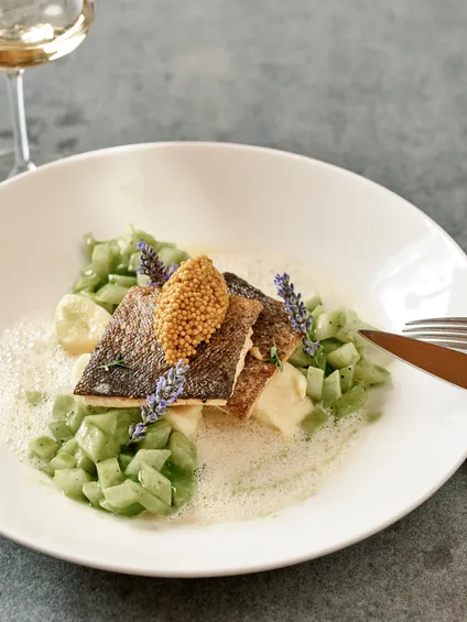 Filetto di pesce gourmet con semi di senape, cubetti di cetriolo e fiori edibili su salsa cremosa