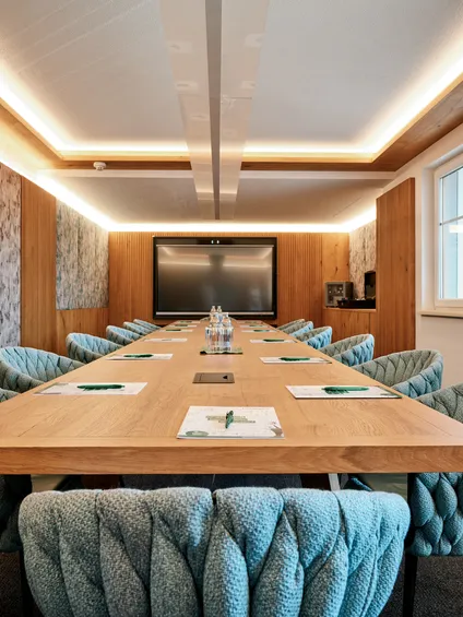 Moderner Konferenzraum mit Holztisch, türkisfarbenen Stühlen und großem Flachbildschirm