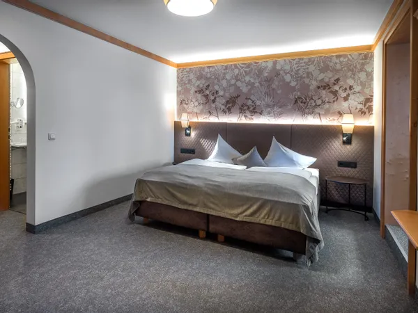Gemütliches Hotelzimmer mit Doppelbett, floralem Kopfteil und sanfter Beleuchtung