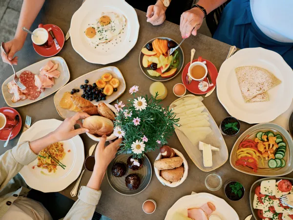 Vielfältiger Frühstückstisch mit Eiern, Käse, Aufschnitt, frischem Obst, Brötchen und Kaffee