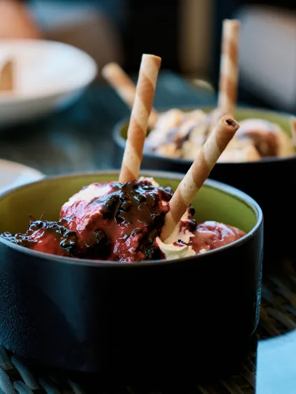 Ciotola di gelato ai frutti di bosco con topping al cioccolato e cannucce wafer su tavolo di vetro