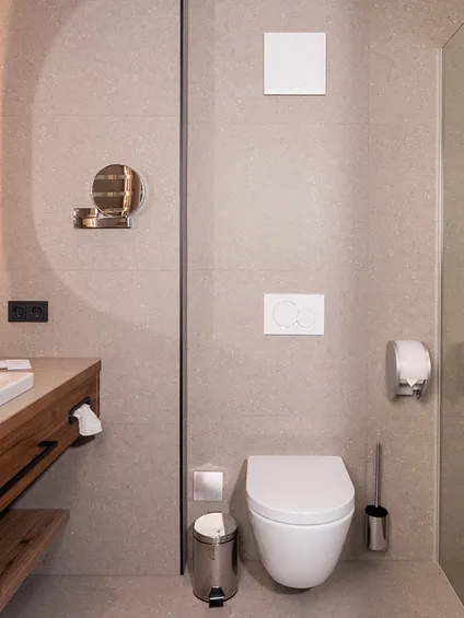 Moderno bagno d'hotel con doccia a filo pavimento, WC sospeso e mobile lavabo in legno con lavabo ampio