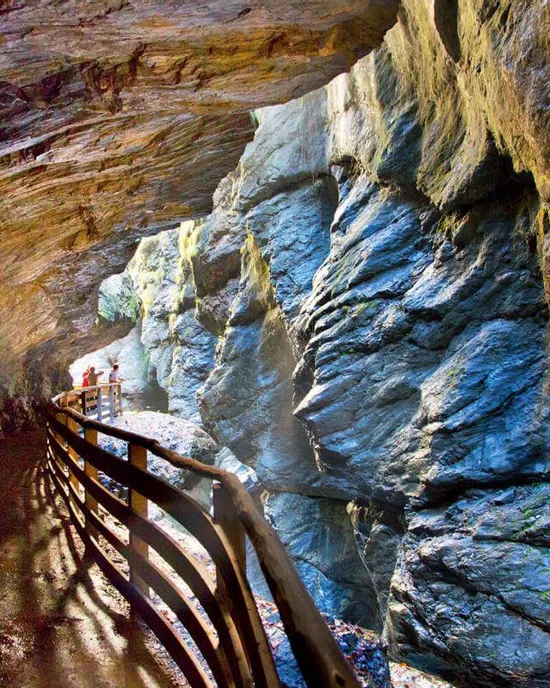Holzsteg durch eine enge felsige Schlucht mit sonnenbeschienenen Steinwänden