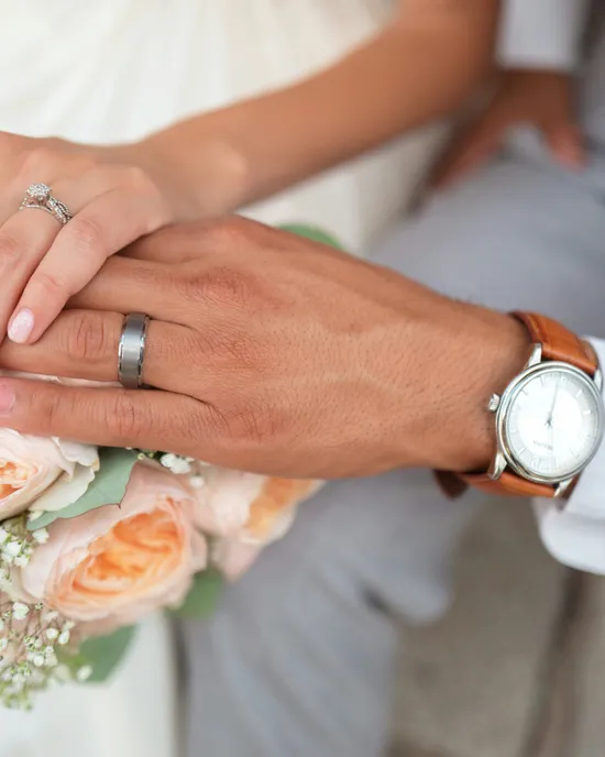 Mani di sposi con fedi nuziali poggiate su un bouquet di rose pesca