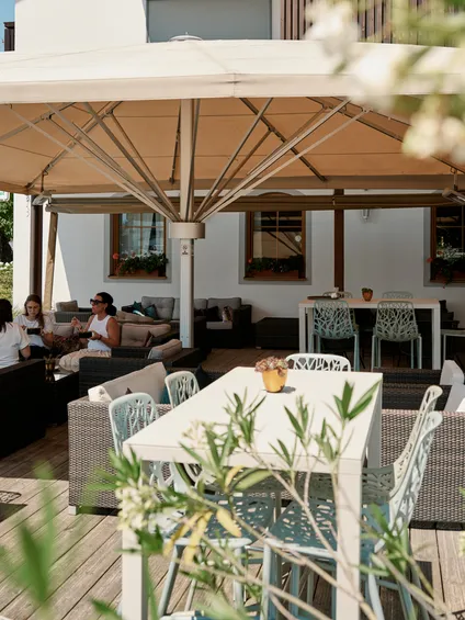Outdoor restaurant terrace with wicker seating and people dining under a large canopy
