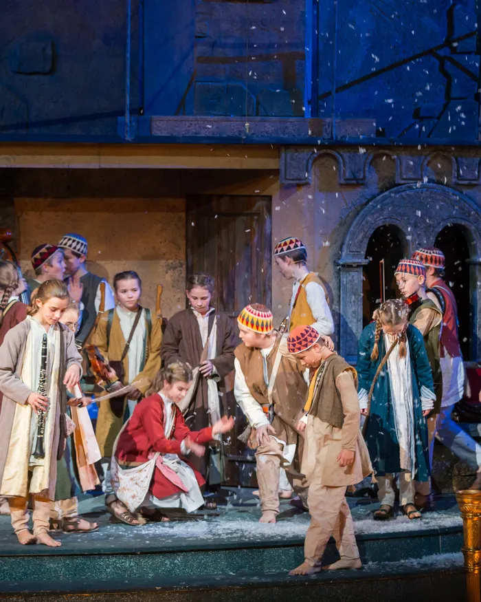 Kinder in bunten Kostümen bei einem Wintertheaterstück mit Musikinstrumenten auf der Bühne