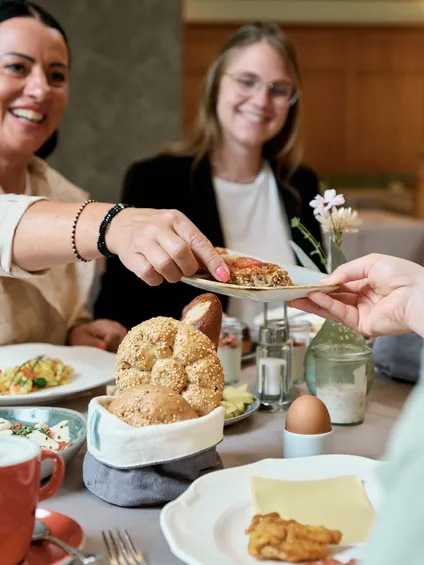 Freunde teilen Essen an einem gemütlichen Frühstückstisch mit Brötchen, Käse und Kaffee