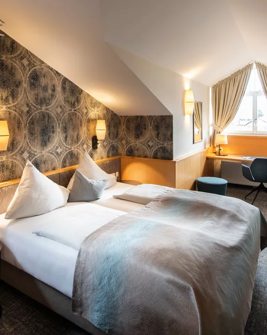 Modernes Hotelzimmer mit Doppelbett, Dachschräge, Schreibtisch am Fenster und Flachbildfernseher