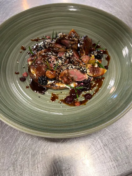 Gourmet-Entenbrust mit Beerensauce, Sesam und Kräutern auf grünem Keramikteller