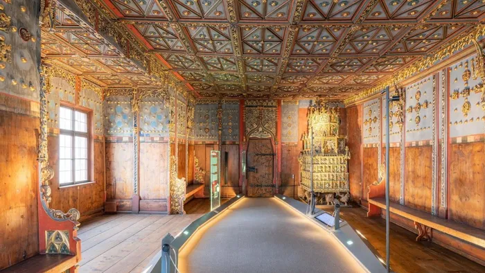 Sala medievale decorata con pareti in legno intagliato, ornamenti dorati e stufa in maiolica