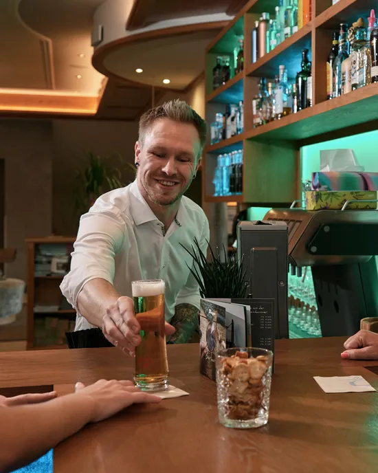 Bartender serving a glass of beer to two smiling women at a modern bar counter