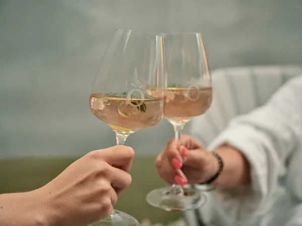 Zwei Personen stoßen mit Gläsern Roséwein in einem Außenbereich an