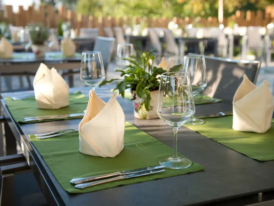Gedeckter Restauranttisch im Freien mit grünen Platzsets, Servietten und leeren Weingläsern