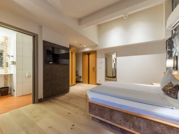 Modernes Hotelzimmer mit Bett, wandmontiertem TV und offener Badezimmertür