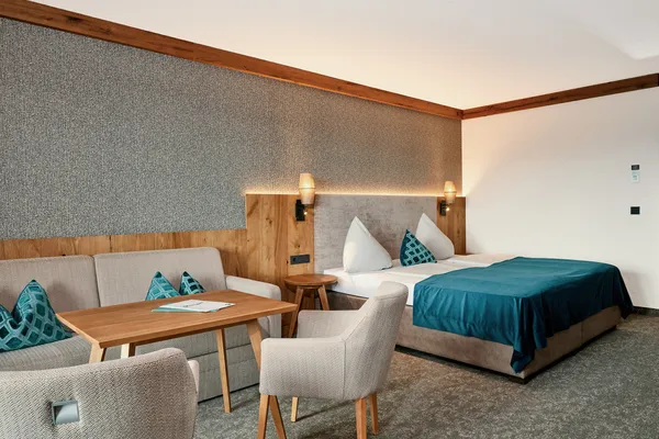 Modernes Hotelzimmer mit Doppelbett, Sofa, Holztisch und türkisfarbenen Akzenten