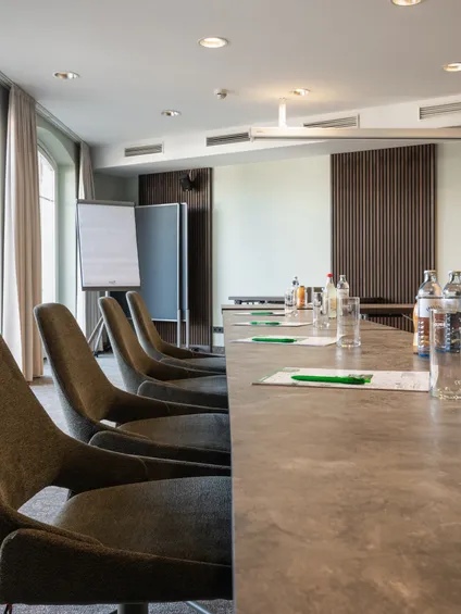 Moderner Konferenzraum mit langem Tisch, Bürostühlen, Schreibblöcken und Wasserflaschen