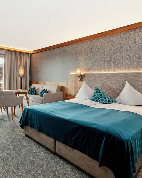 Moderna camera d'albergo con letto matrimoniale, area salotto e accesso al balcone