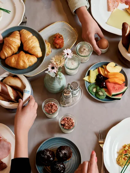 Tavola da brunch con croissant, frutta, formaggi, pane, uova, caffè e piatti da colazione assortiti