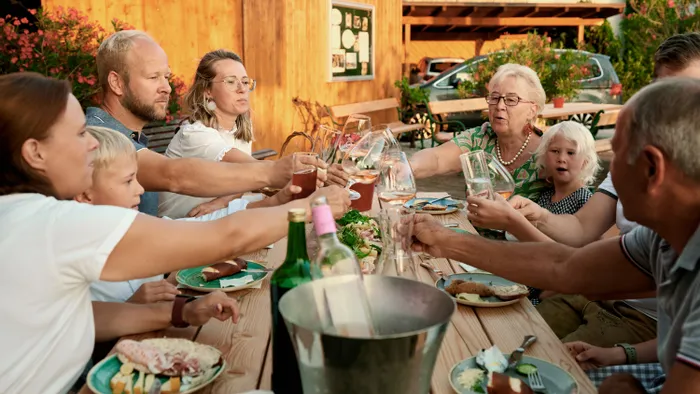 Family and friends toasting drinks at a wooden outdoor table with food in a rustic setting