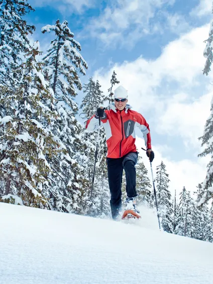 Uomo con racchette da neve in discesa tra alberi innevati in una giornata invernale soleggiata