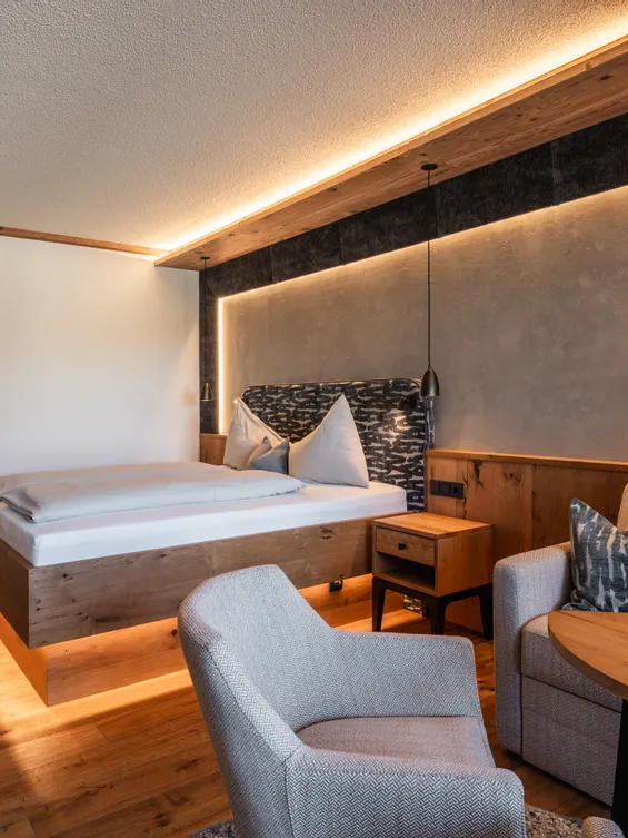 Modernes Hotelzimmer mit Holzmöbeln, gemütlichem Bett, Sofa, Sessel und stimmungsvoller Beleuchtung