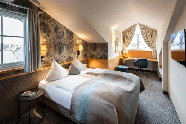 Modernes Hotelzimmer mit Doppelbett, Dachschräge, Schreibtisch am Fenster und Flachbildfernseher