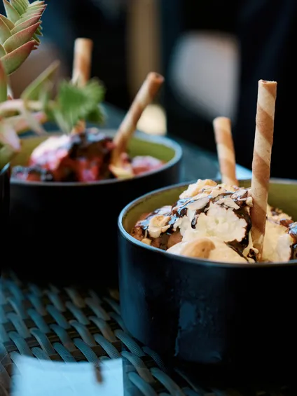 Schüssel mit Vanilleeis, Schlagsahne, Schokosirup und Waffelröllchen auf Glastisch