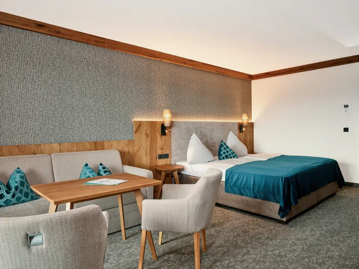 Modernes Hotelzimmer mit Doppelbett, Sofa, Holztisch und türkisfarbenen Akzenten